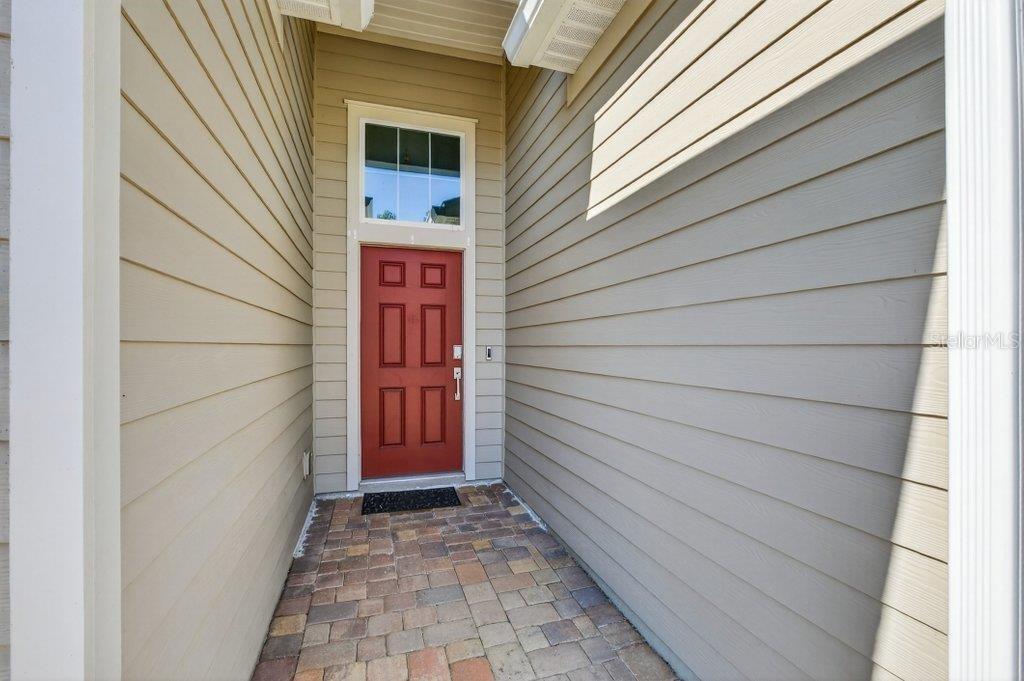 A red front door is set within a covered entryway with light-colored horizontal siding — 210 WHITE RABBIT RUN, ST AUGUSTINE, FL