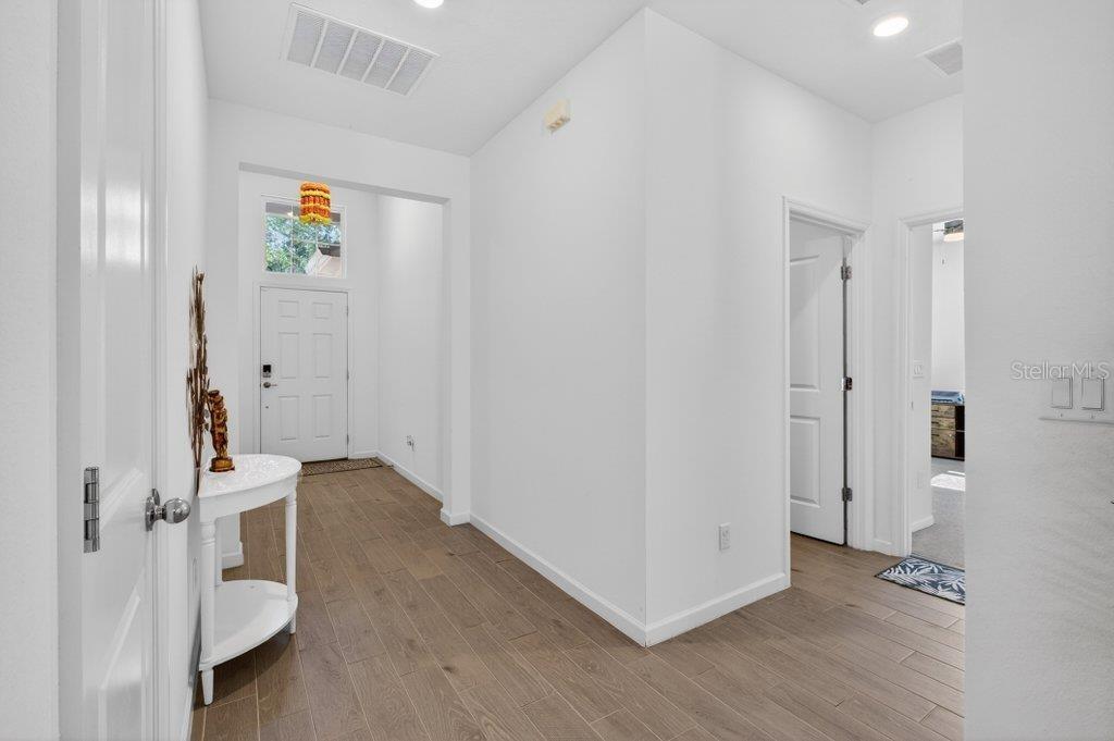 An entryway with light wood-look flooring, white walls, and a white front door — 210 WHITE RABBIT RUN, ST AUGUSTINE, FL