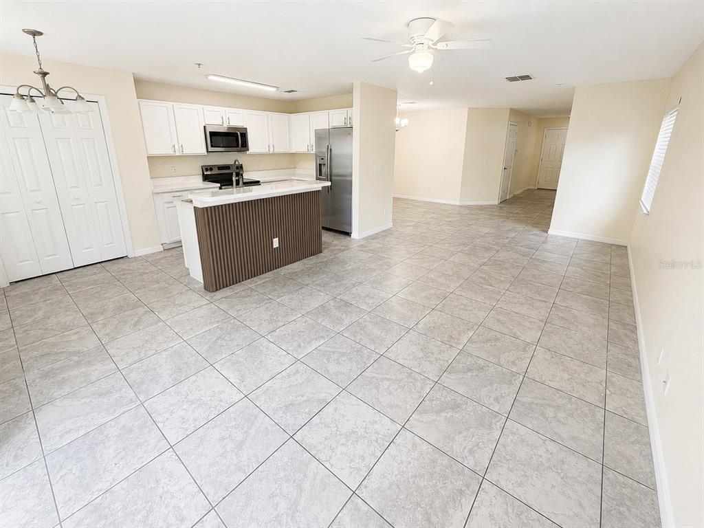 A kitchen with white cabinets and a wood-paneled island opens into a tiled living area — 13507 TEA ROSE WAY UNIT 128, ORLANDO, FL