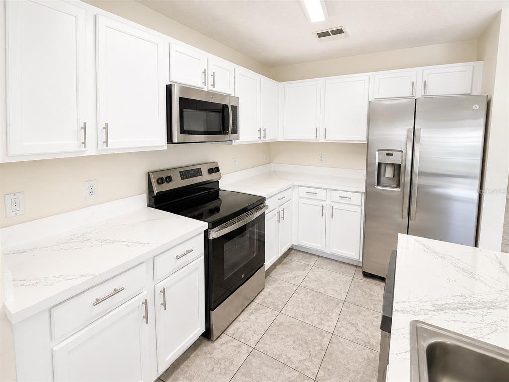 A kitchen with white cabinets, stainless steel appliances, and white countertops with grey veining — 13507 TEA ROSE WAY UNIT 128, ORLANDO, FL