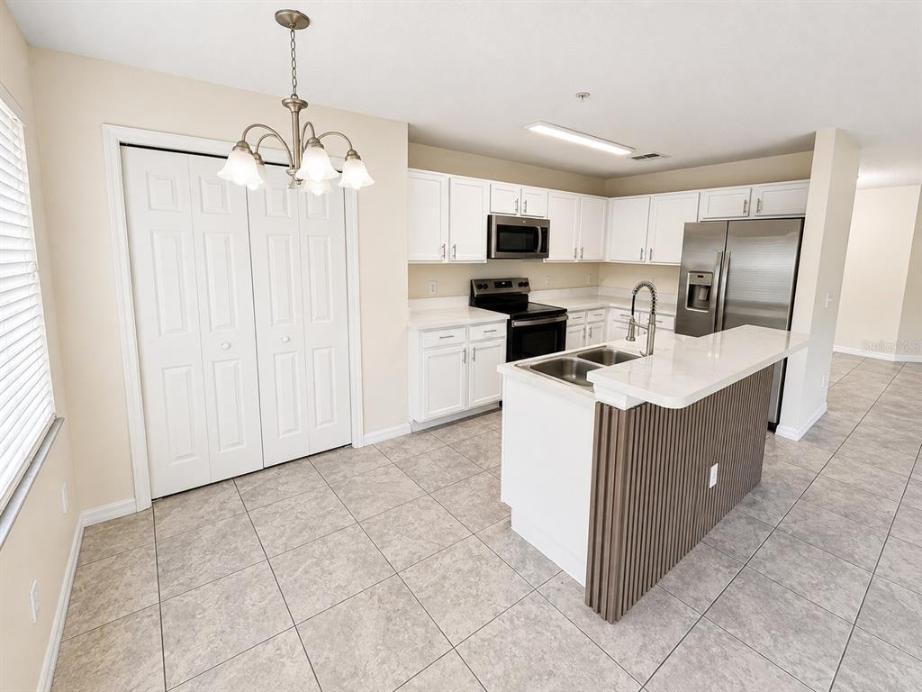A kitchen features white cabinets, stainless steel appliances, a center island, and light tile flooring — 13507 TEA ROSE WAY UNIT 128, ORLANDO, FL