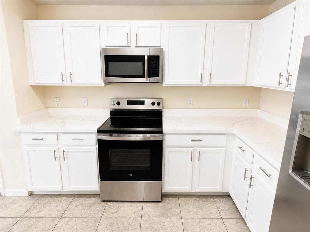 A kitchen with white cabinets, stainless steel appliances, and light-colored countertops — 13507 TEA ROSE WAY UNIT 128, ORLANDO, FL