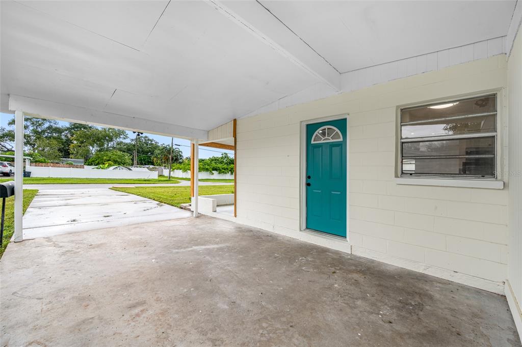 A covered concrete carport features a teal front door and a single window — 8176 65TH STREET N, PINELLAS PARK, FL