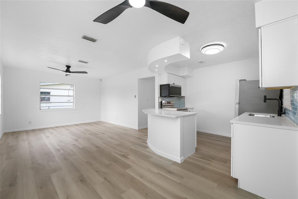 An open-concept kitchen and living area with white cabinets, light wood floors, and ceiling fans — 8176 65TH STREET N, PINELLAS PARK, FL