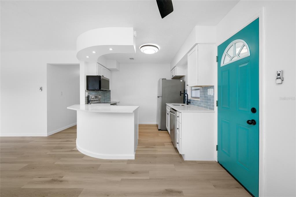 A kitchen with white cabinets, a curved breakfast bar, and a bright teal front door — 8176 65TH STREET N, PINELLAS PARK, FL