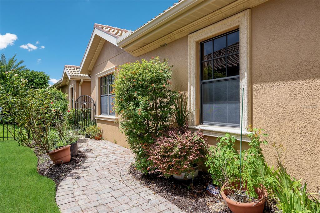 A paved walkway leads along the side of a tan stucco house with two windows — 6123 25TH STREET E, ELLENTON, FL