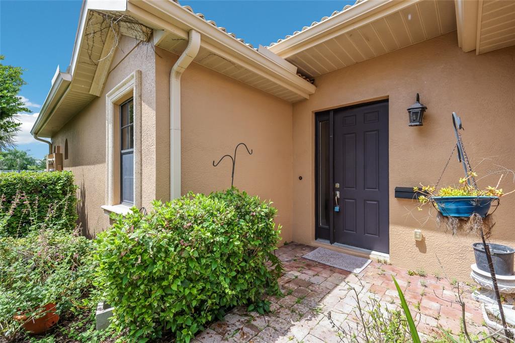 A tan house exterior features a dark front door, brick walkway, and a hanging plant — 6123 25TH STREET E, ELLENTON, FL