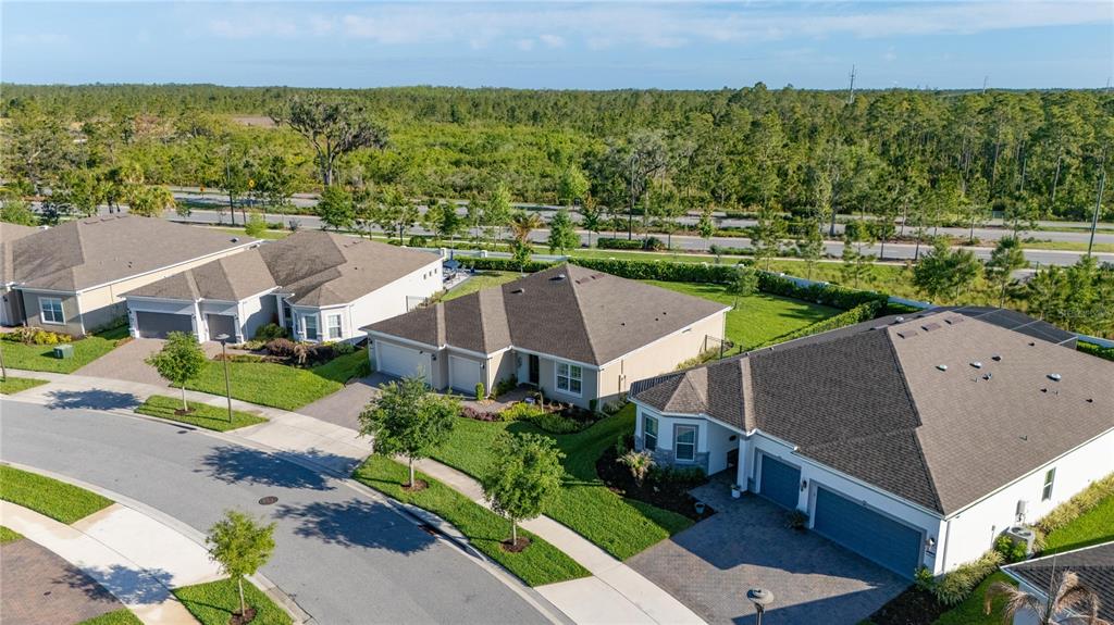 An aerial view shows three suburban houses with driveways and lawns near a wooded area — 2873 CHERRY BLOSSOM LOOP, ST CLOUD, FL
