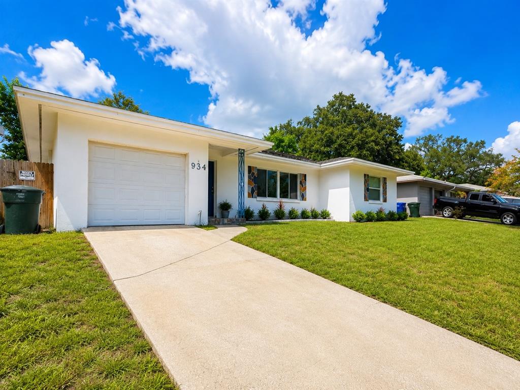 A white single-story house features a concrete driveway, a garage, and a green lawn — 934 HILLWOOD DR, DUNEDIN, FL