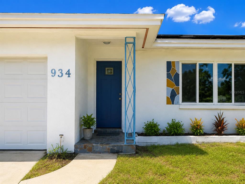 The exterior of a white house features a blue front door and a decorative metal post — 934 HILLWOOD DR, DUNEDIN, FL