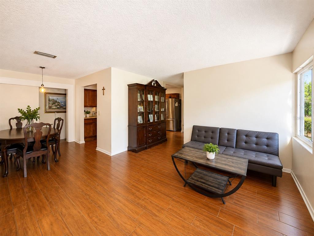 A living and dining area features wood-look tile flooring, a dark hutch, and a black sofa — 934 HILLWOOD DR, DUNEDIN, FL