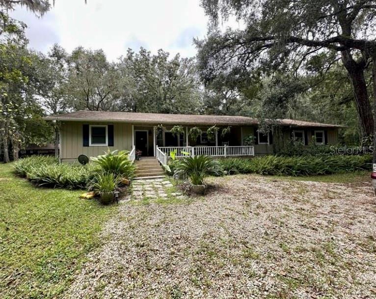 A single-story house with a covered porch and gravel driveway surrounded by mature trees — 24392 LANARK ROAD, BROOKSVILLE, FL
