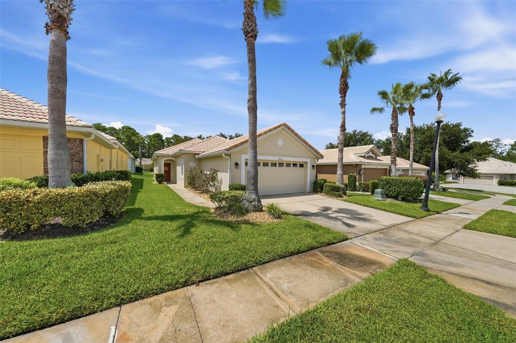 A single-story tan house with a two-car garage and palm trees in the front yard — 9076 SAINT ANDREWS WAY, MOUNT DORA, FL