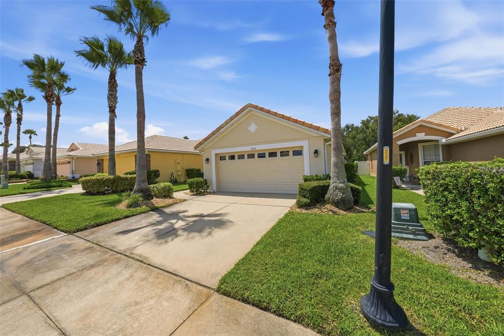 A single-story house with a beige exterior, a two-car garage, and palm trees in front — 9076 SAINT ANDREWS WAY, MOUNT DORA, FL