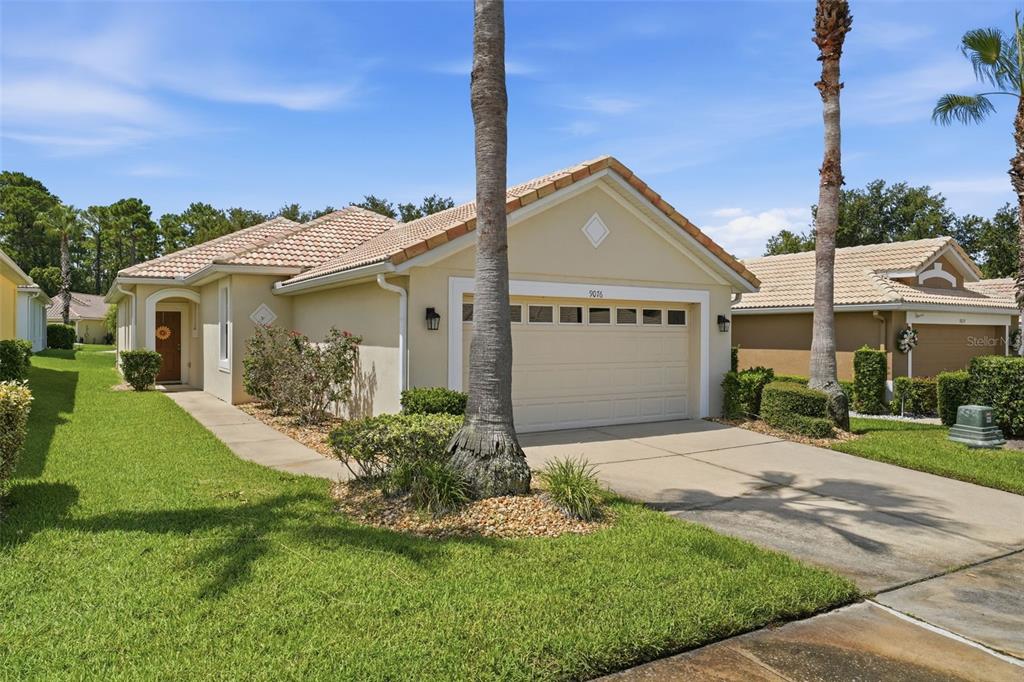 A single-story house with a beige stucco exterior, a tile roof, and a two-car garage — 9076 SAINT ANDREWS WAY, MOUNT DORA, FL