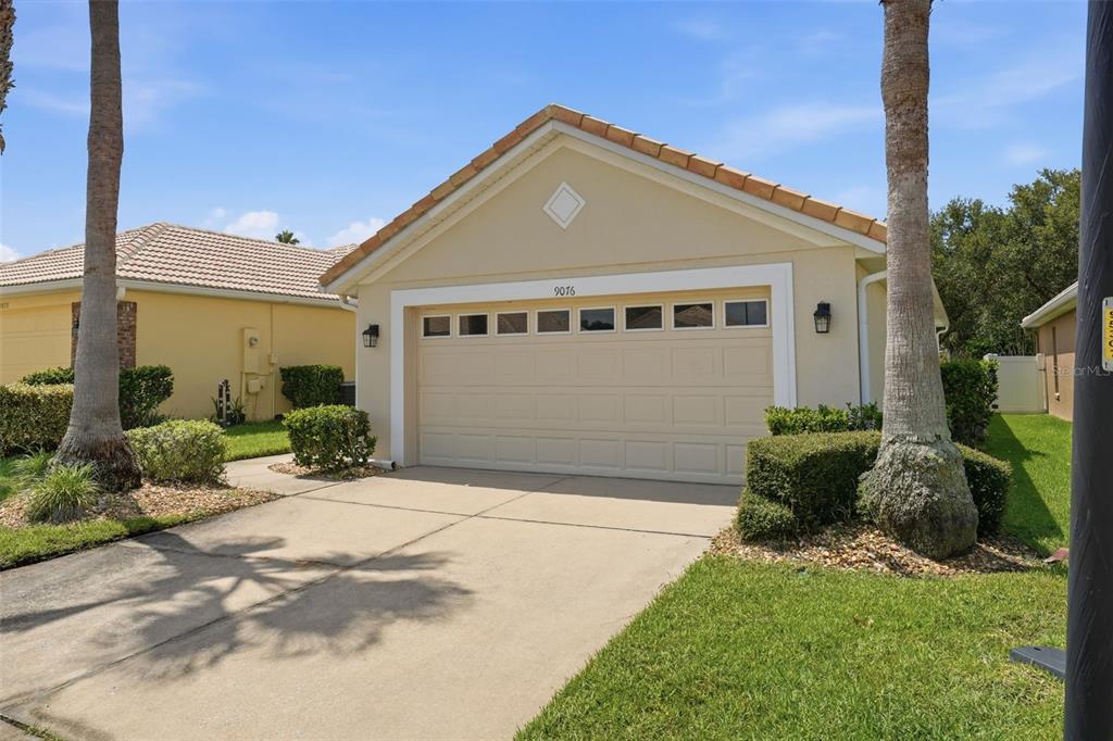 A beige single-story house with a two-car garage and a concrete driveway — 9076 SAINT ANDREWS WAY, MOUNT DORA, FL