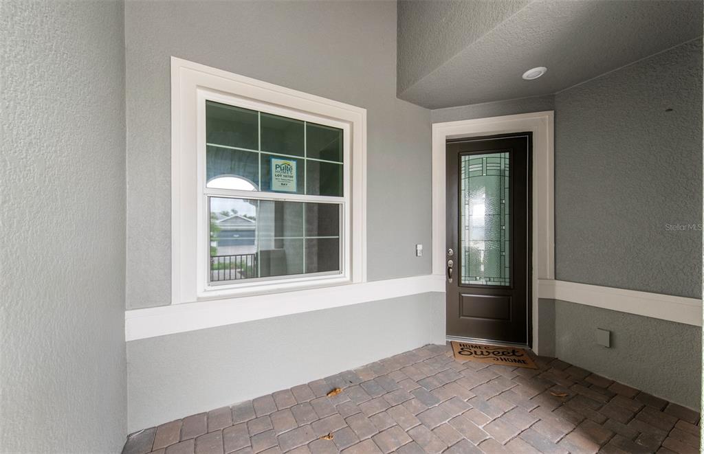 A covered entryway features a brown front door, a large window, and brick paver flooring — 1611 TAVIRA PLACE, ENGLEWOOD, FL