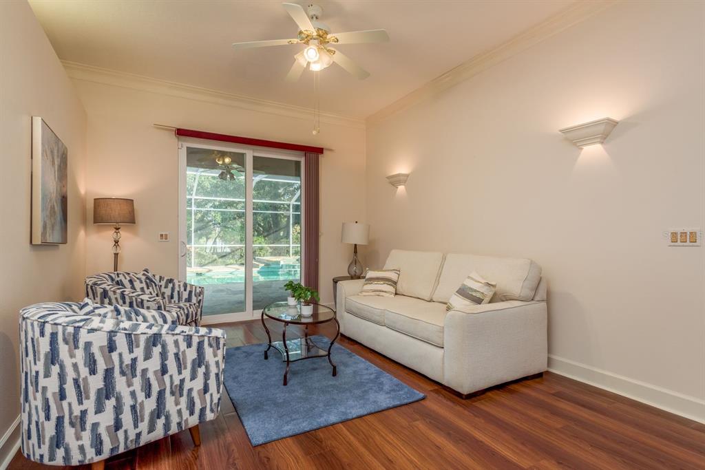 A living room features a sofa, patterned armchairs, a blue rug, and sliding glass doors — 771 WEATHERSFIELD DRIVE, DUNEDIN, FL
