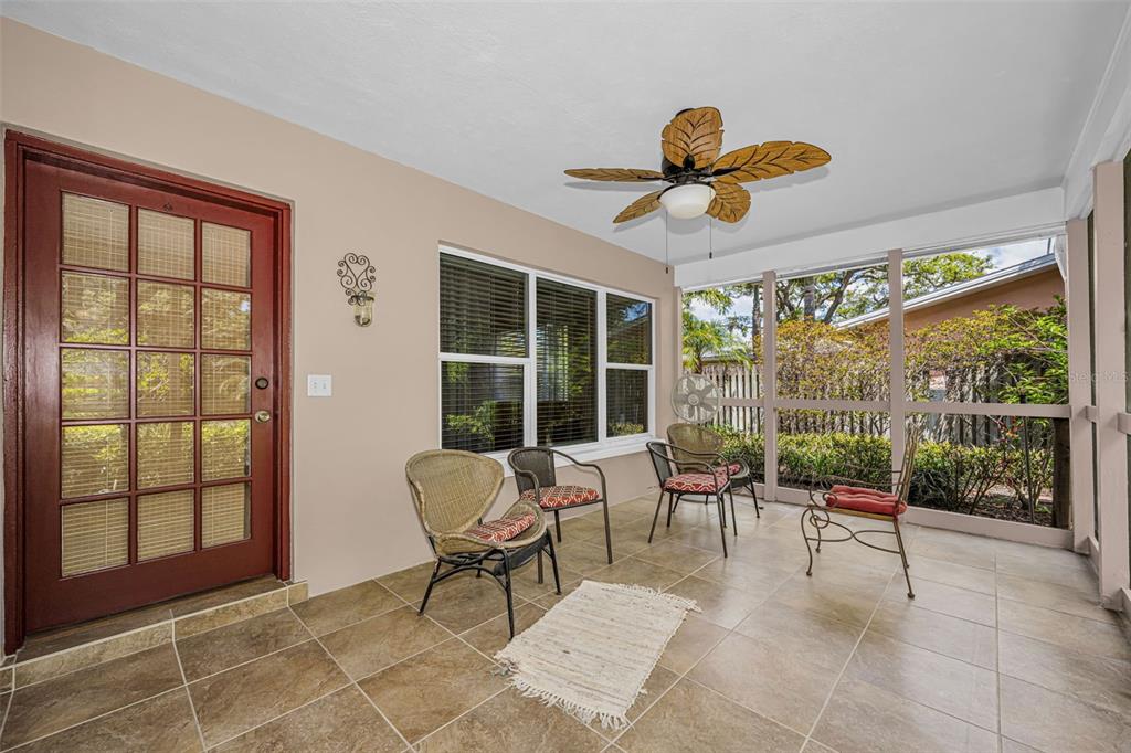 A screened-in porch with tile flooring, four chairs, a ceiling fan, and a glass door — 253 PARK CIRCLE S, DUNEDIN, FL