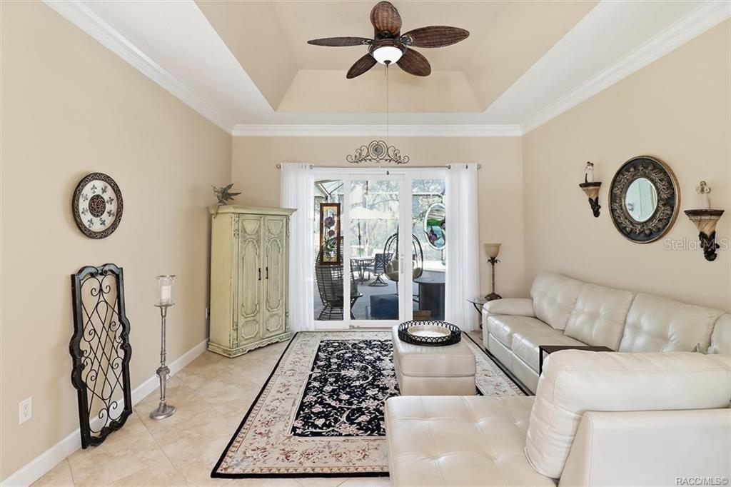 A living room features a tray ceiling, tile flooring, a white sofa, and sliding glass doors — 3033 N CAVES VALLEY PATH, LECANTO, FL