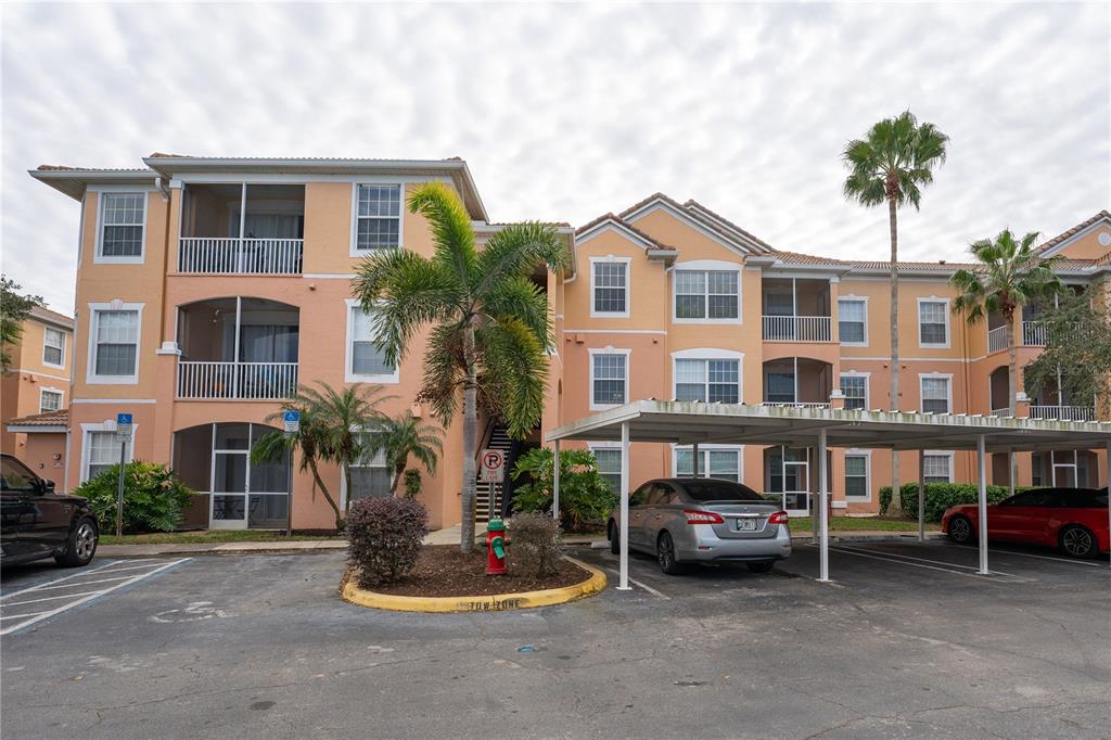 A multi-story apartment building with a parking lot and covered carports in front — 13536 TURTLE MARSH LOOP UNIT 523, ORLANDO, FL