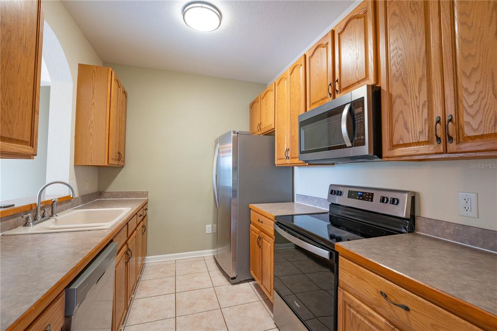 A galley kitchen features oak cabinets, stainless steel appliances, and beige tile flooring — 13536 TURTLE MARSH LOOP UNIT 523, ORLANDO, FL