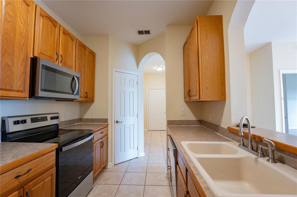 A kitchen features oak cabinets, laminate countertops, a double sink, and stainless steel appliances — 13536 TURTLE MARSH LOOP UNIT 523, ORLANDO, FL
