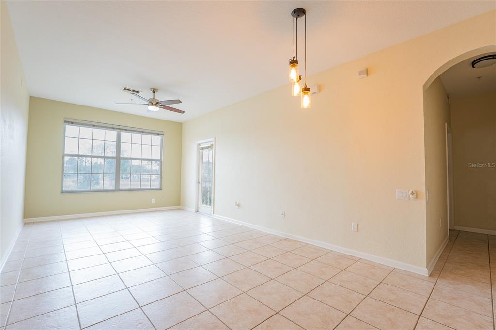 An empty living room features tile flooring, a ceiling fan, and a three-light pendant fixture — 13536 TURTLE MARSH LOOP UNIT 523, ORLANDO, FL