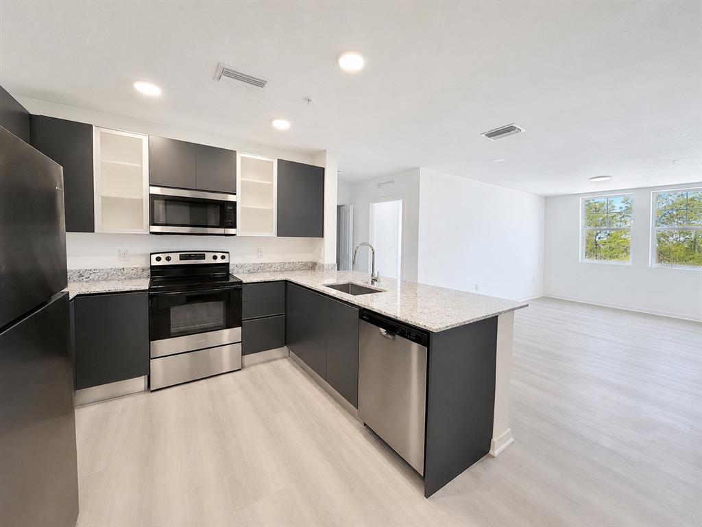 An open-concept living area features light wood-look flooring and a view into the kitchen — 5587 MILLENIA PARK BOULEVARD UNIT 316, ORLANDO, FL