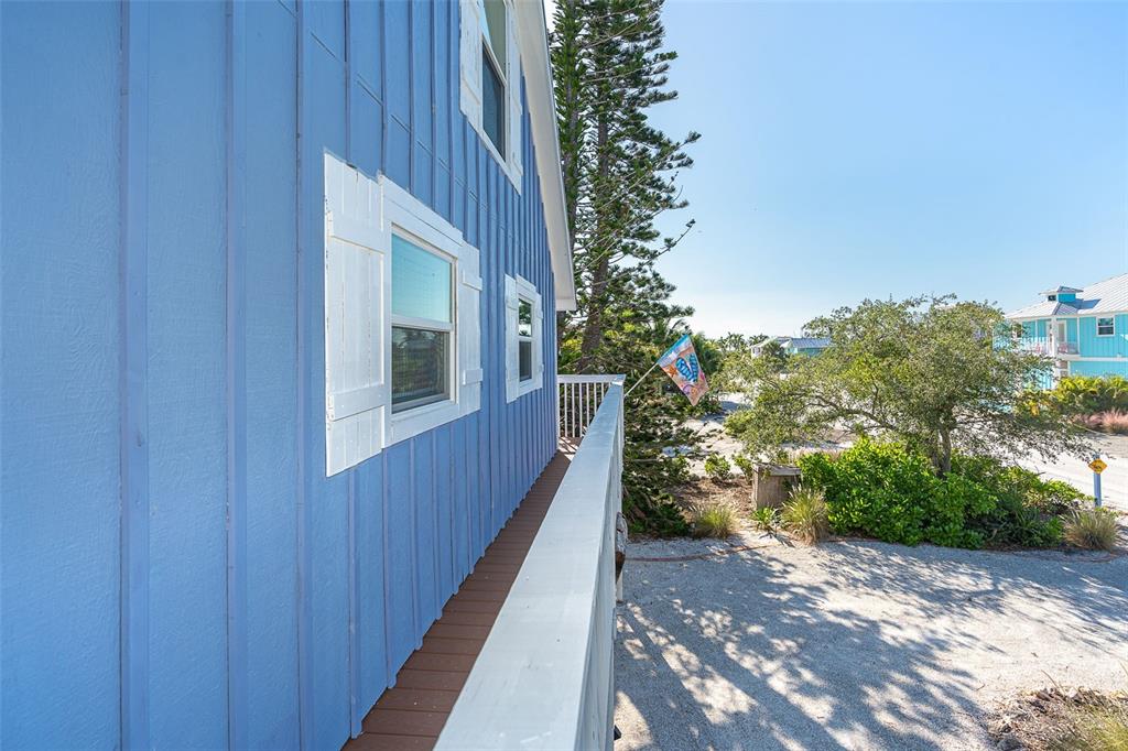 A blue house exterior features a wooden balcony overlooking a gravel driveway and trees — 210 BOCILLA DRIVE, PLACIDA, FL