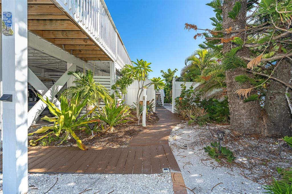 A wooden walkway leads through a landscaped yard under an elevated house with white pillars — 210 BOCILLA DRIVE, PLACIDA, FL