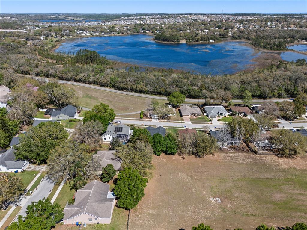 An aerial view shows a residential neighborhood with houses bordering a large lake and field — 834 HIGH POINTE CIRCLE, MINNEOLA, FL
