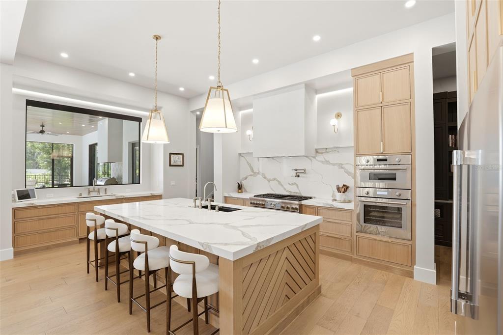 A modern kitchen features a large marble-topped island, light wood cabinetry, and stainless steel appliances — 1206 SUTTER AVENUE, GOTHA, FL