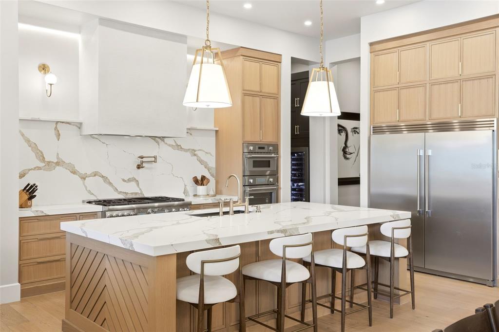 A modern kitchen features a marble-topped island, light wood cabinetry, and stainless steel appliances — 1206 SUTTER AVENUE, GOTHA, FL