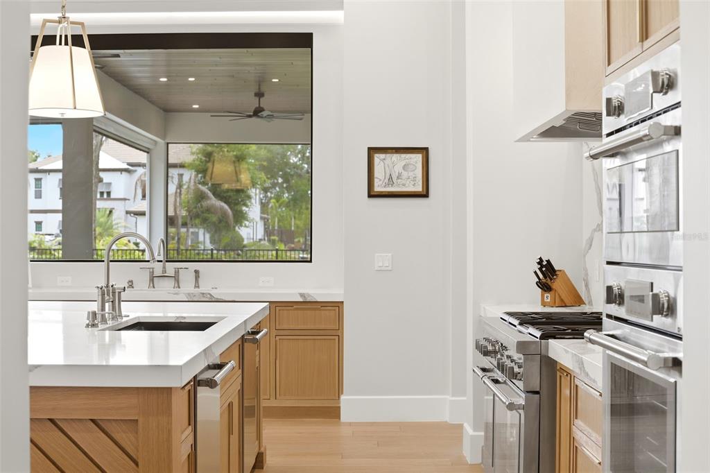 A modern kitchen features light wood cabinets, white countertops, stainless steel appliances, and a large window — 1206 SUTTER AVENUE, GOTHA, FL