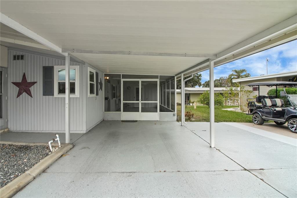 A covered carport leads to a screened-in porch entrance of a light gray mobile home — 11 ORANGEWOOD DRIVE, FRUITLAND PARK, FL