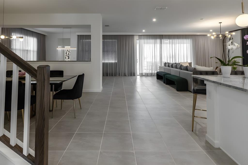 An open-concept living and dining area features large gray floor tiles and floor-to-ceiling curtains — 9199 BREEZE MIST TERRACE, DAVENPORT, FL