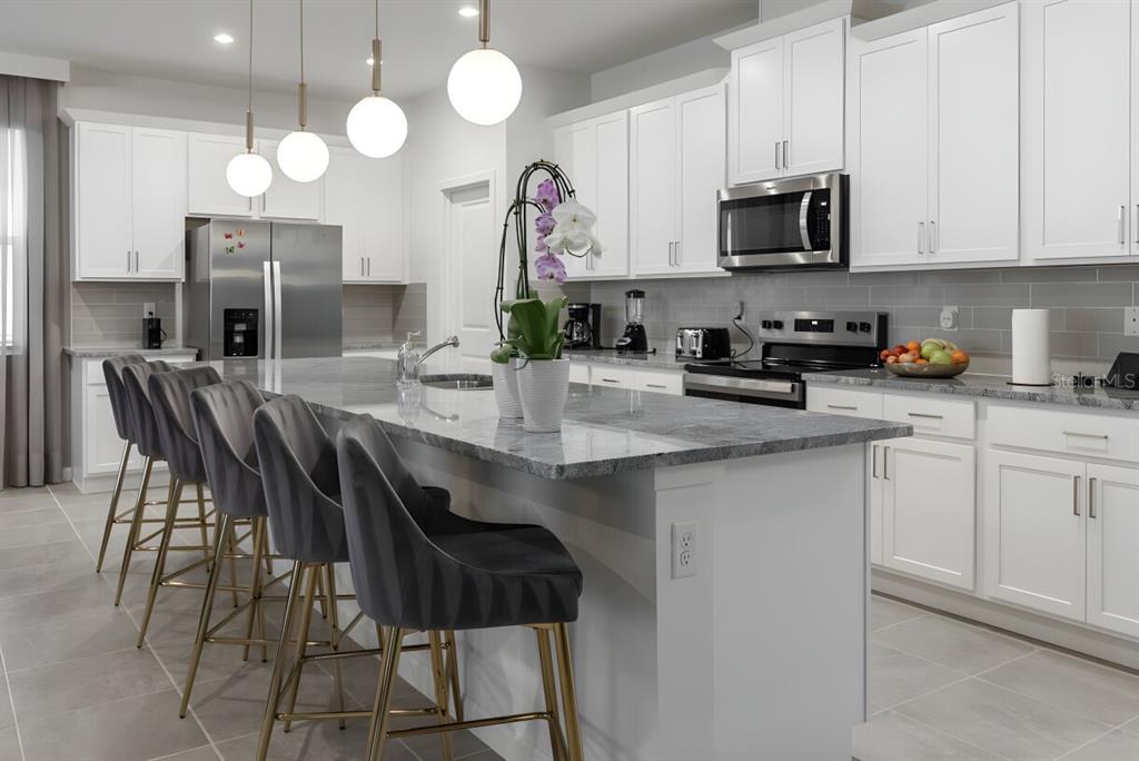 A modern kitchen features white cabinetry, a large granite island, and four gray bar stools — 9199 BREEZE MIST TERRACE, DAVENPORT, FL