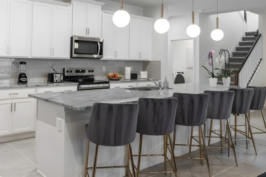 A modern kitchen features white cabinets, a gray granite island, and four gray velvet barstools — 9199 BREEZE MIST TERRACE, DAVENPORT, FL