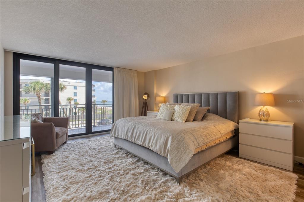 A bedroom features a king bed, a shaggy rug, and a balcony overlooking the ocean — 1239 OCEAN SHORE BOULEVARD UNIT 2E5, ORMOND BEACH, FL
