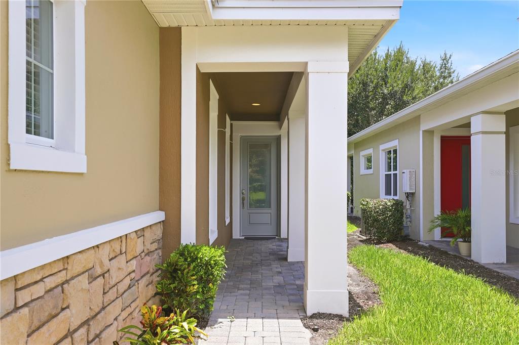 A paved walkway leads to a covered entryway with a gray door and stone accents — 2447 YELLOW BRICK ROAD, ST CLOUD, FL