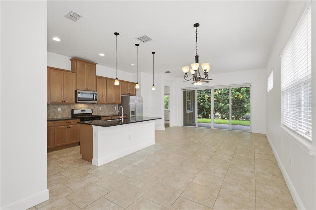 A kitchen with wood cabinets and a granite island opens to a dining area — 2447 YELLOW BRICK ROAD, ST CLOUD, FL