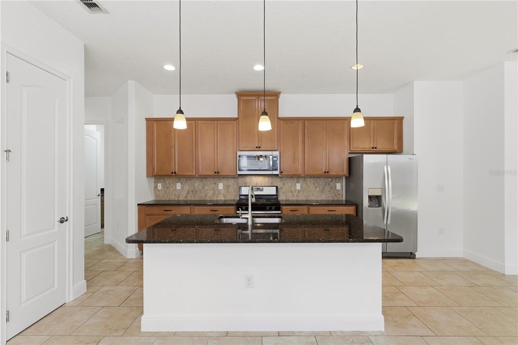 A kitchen features wood cabinets, dark granite countertops, a central island, and stainless steel appliances — 2447 YELLOW BRICK ROAD, ST CLOUD, FL