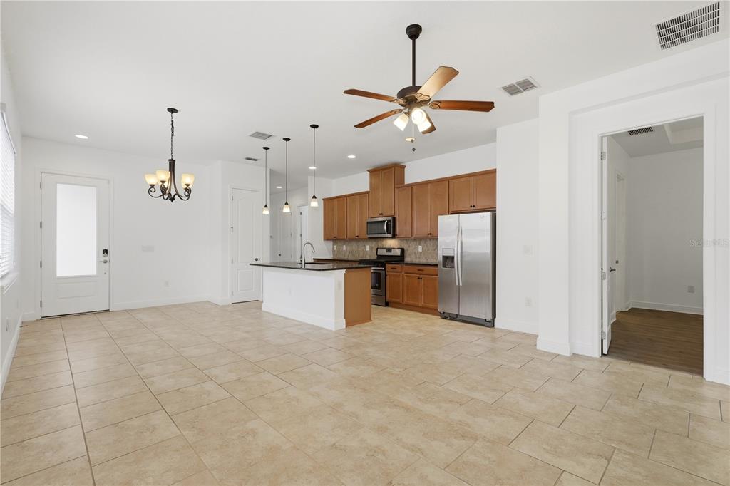 An open-concept kitchen features wood cabinets, stainless steel appliances, a center island, and tile flooring — 2447 YELLOW BRICK ROAD, ST CLOUD, FL