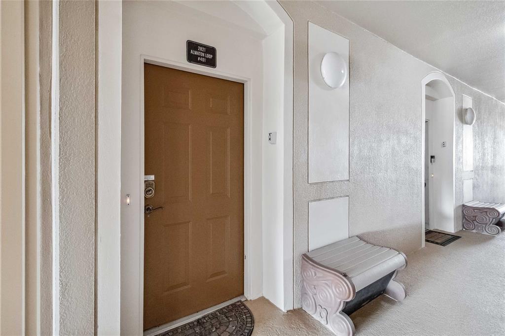 A brown apartment door with a keypad lock sits in a beige hallway with benches — 2821 E ALMATON LOOP UNIT 401, KISSIMMEE, FL