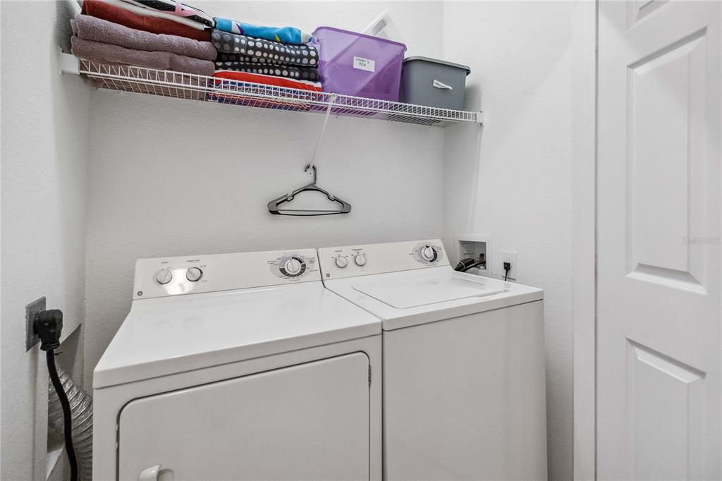 A laundry room features a white washer and dryer set beneath a wire storage shelf — 2821 E ALMATON LOOP UNIT 401, KISSIMMEE, FL