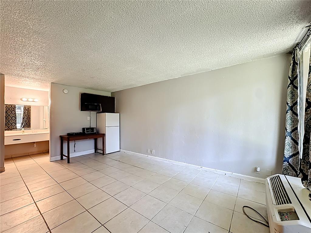 A room with tiled floors, a small kitchenette area, and a wall-mounted air conditioning unit — 7900 S ORANGE BLOSSOM TRAIL UNIT 1108, ORLANDO, FL