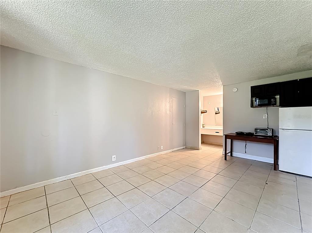 A room with light-colored tile flooring, gray walls, a small kitchenette area, and a bathroom — 7900 S ORANGE BLOSSOM TRAIL UNIT 1108, ORLANDO, FL