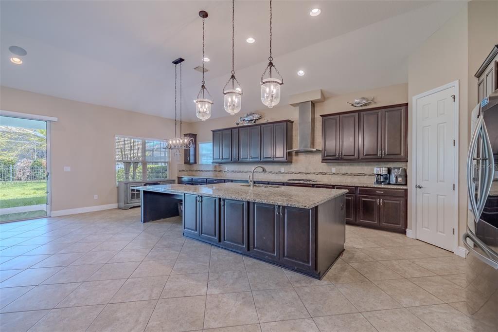 A kitchen features dark wood cabinets, granite countertops, a large island, and tile flooring — 5927 JASPER GLEN DRIVE, LITHIA, FL