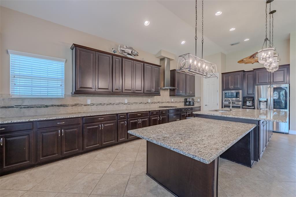 A kitchen features dark wood cabinets, granite countertops, a large island, and tile flooring — 5927 JASPER GLEN DRIVE, LITHIA, FL